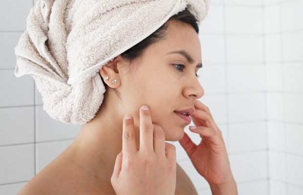 woman standing in the shower touching her face and concerned for her skin